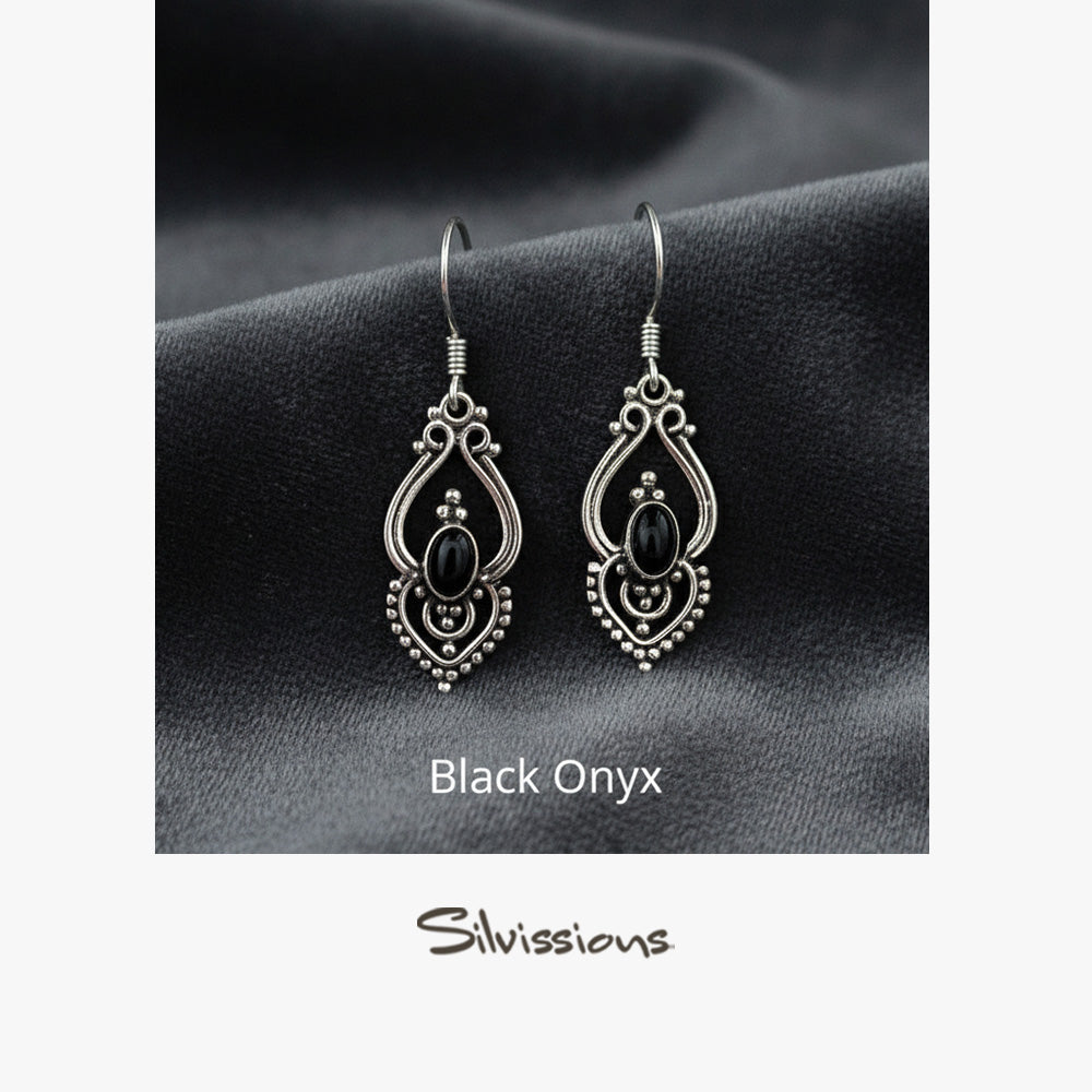 Pair of silver earrings with black gemstones on a gray fabric background, branded 'Silvissions'.