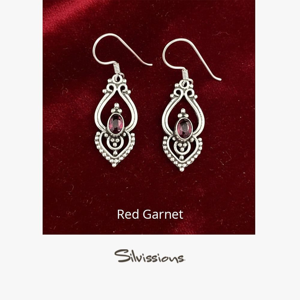 A pair of sterling silver dangle earrings with red garnet oval gemstones, displayed against a backdrop.