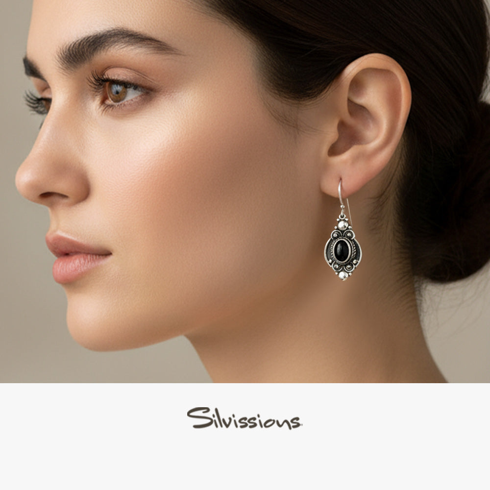 Woman wearing a silver earring with a black gemstone, branded 'Silvassions'.