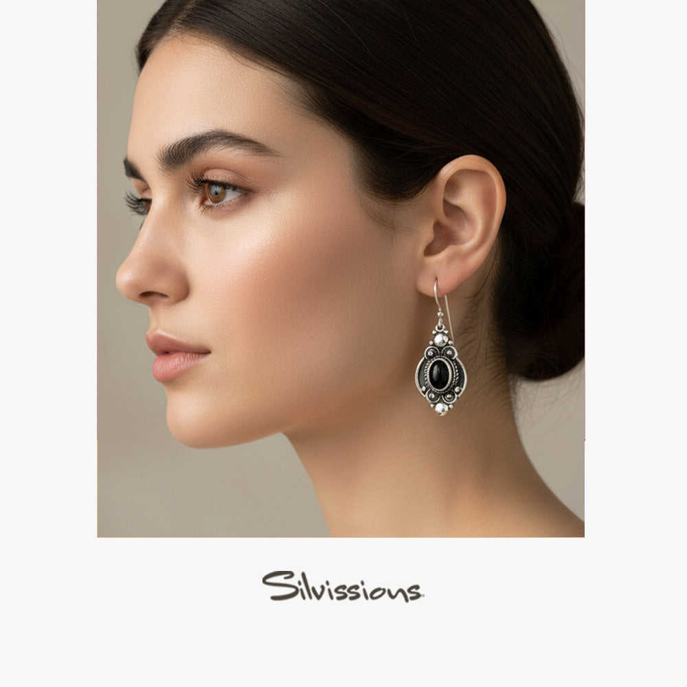 Woman wearing a silver earring with a black gemstone, branded 'Silvassions'.