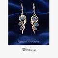 Silver earrings with rainbow moonstone stones on a blue satin background, branded 'Silvissions'.