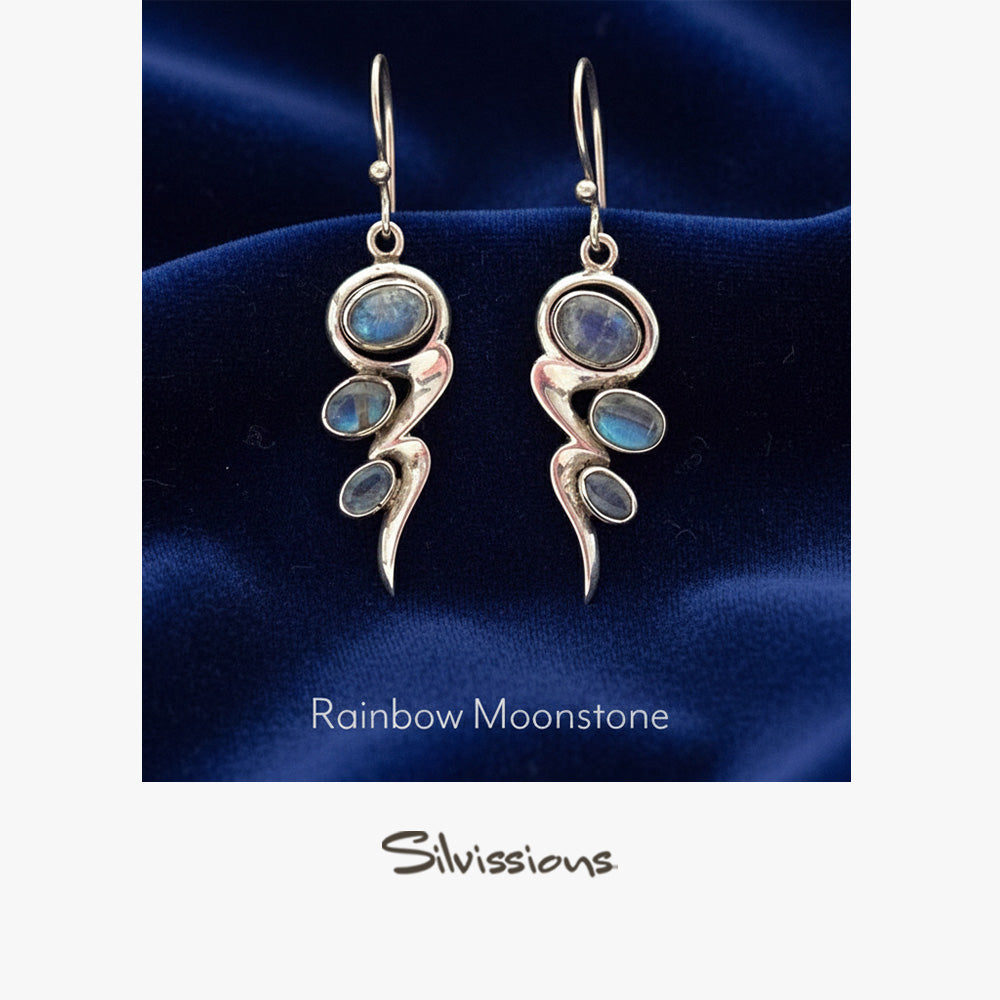 Silver earrings with rainbow moonstone stones on a blue satin background, branded 'Silvissions'.