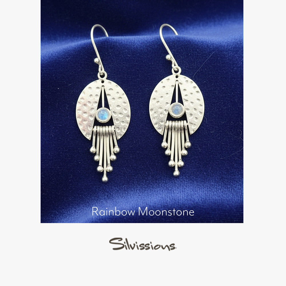 Silver earrings with rainbow moonstone on a blue satin background, branded 'Silvissions'.