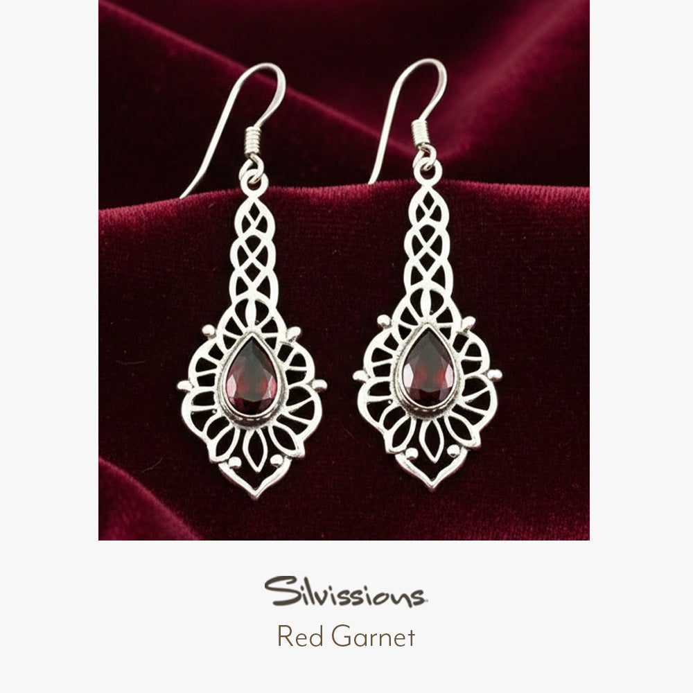 Silver earrings with red gemstones on a red fabric background, branded 'Silvissions'.