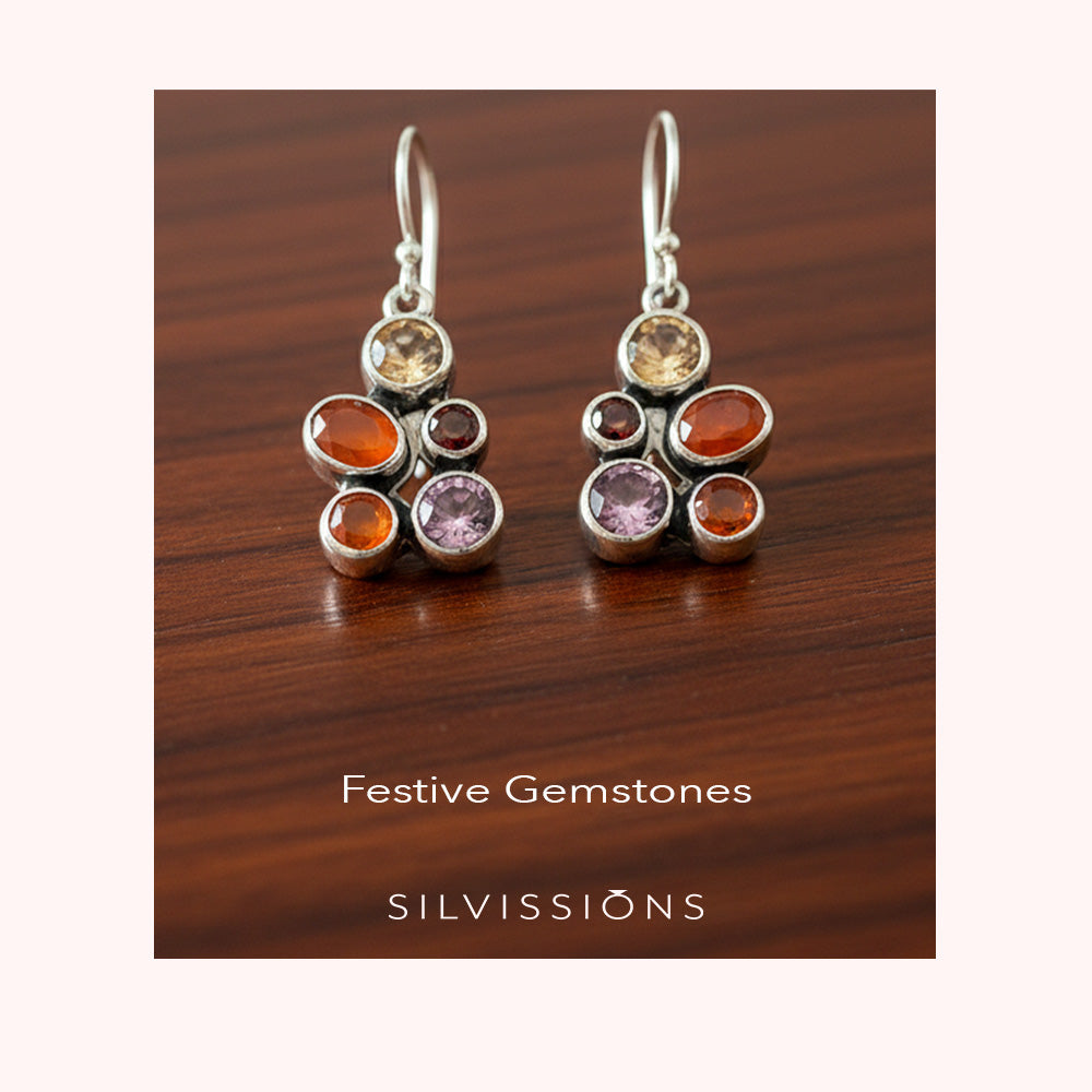 Pair of earrings with colorful gemstones on a blurred background, featuring the brand 'Silvissions'.