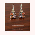 Pair of earrings with colorful gemstones on a blurred background, featuring the brand 'Silvissions'.