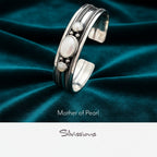 Silver bracelet with mother of pearl stones on a blurred background with tea set and flowers.
