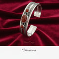 Silver bracelet with red onyx stones on a wooden surface with flowers in the background, branded 'Silvissions'.