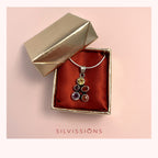 A silver pendant necklace with multiple colorful gemstones is displayed inside an open gold jewelry box lined with red satin. The brand name 'SILVISSIONS' is printed in red at the bottom of the image against a light pink background.