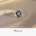 Silver ring with an oval-shaped rainbow moonstone on a soft fabric background, featuring the brand 'Silvissions'.