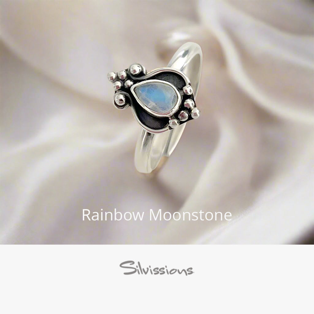 Silver ring with a heart-shaped rainbow moonstone on a soft fabric background, featuring the brand 'Silvissions'.