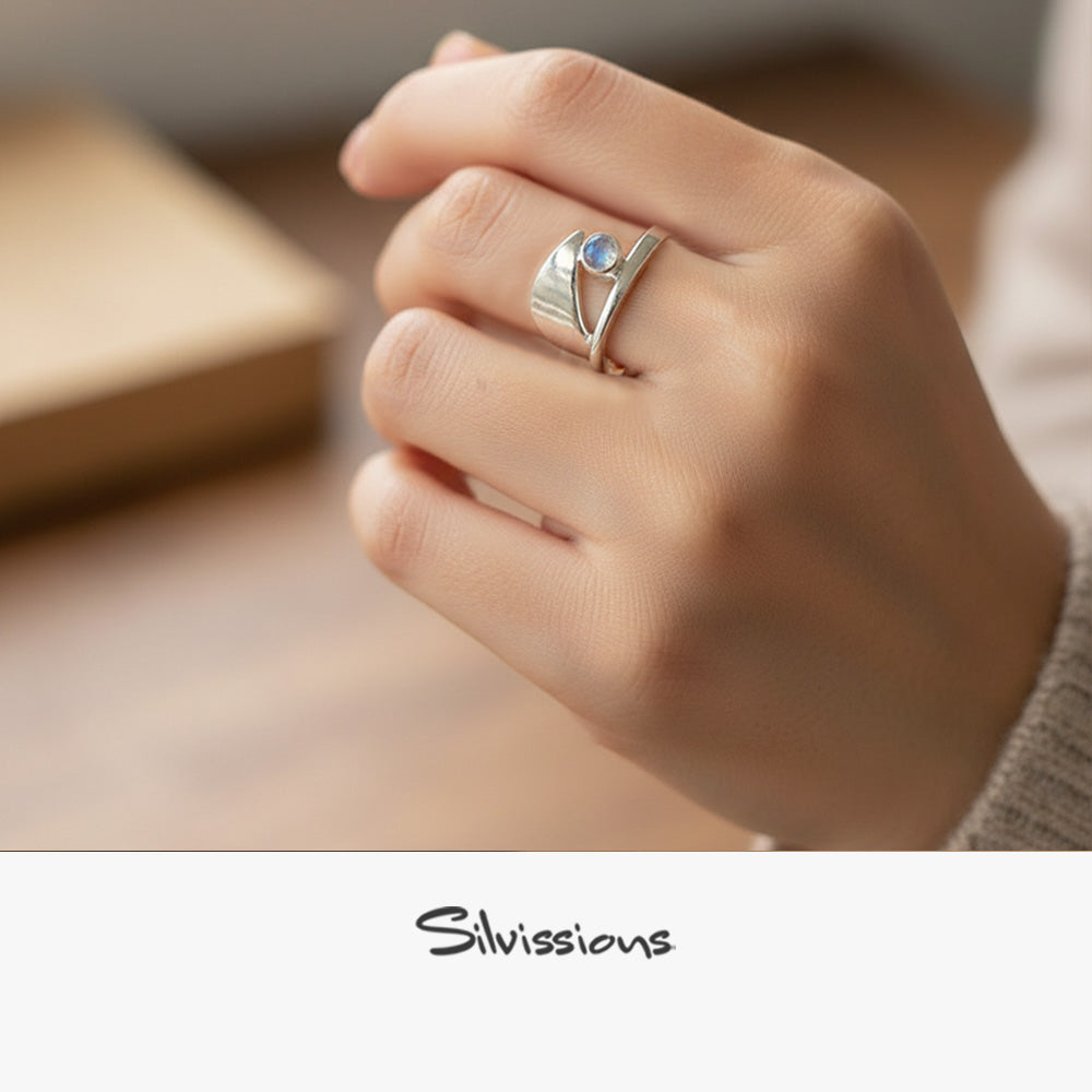 Hand wearing a silver ring with a blue gemstone on a neutral background, featuring the brand 'Silvissions'.