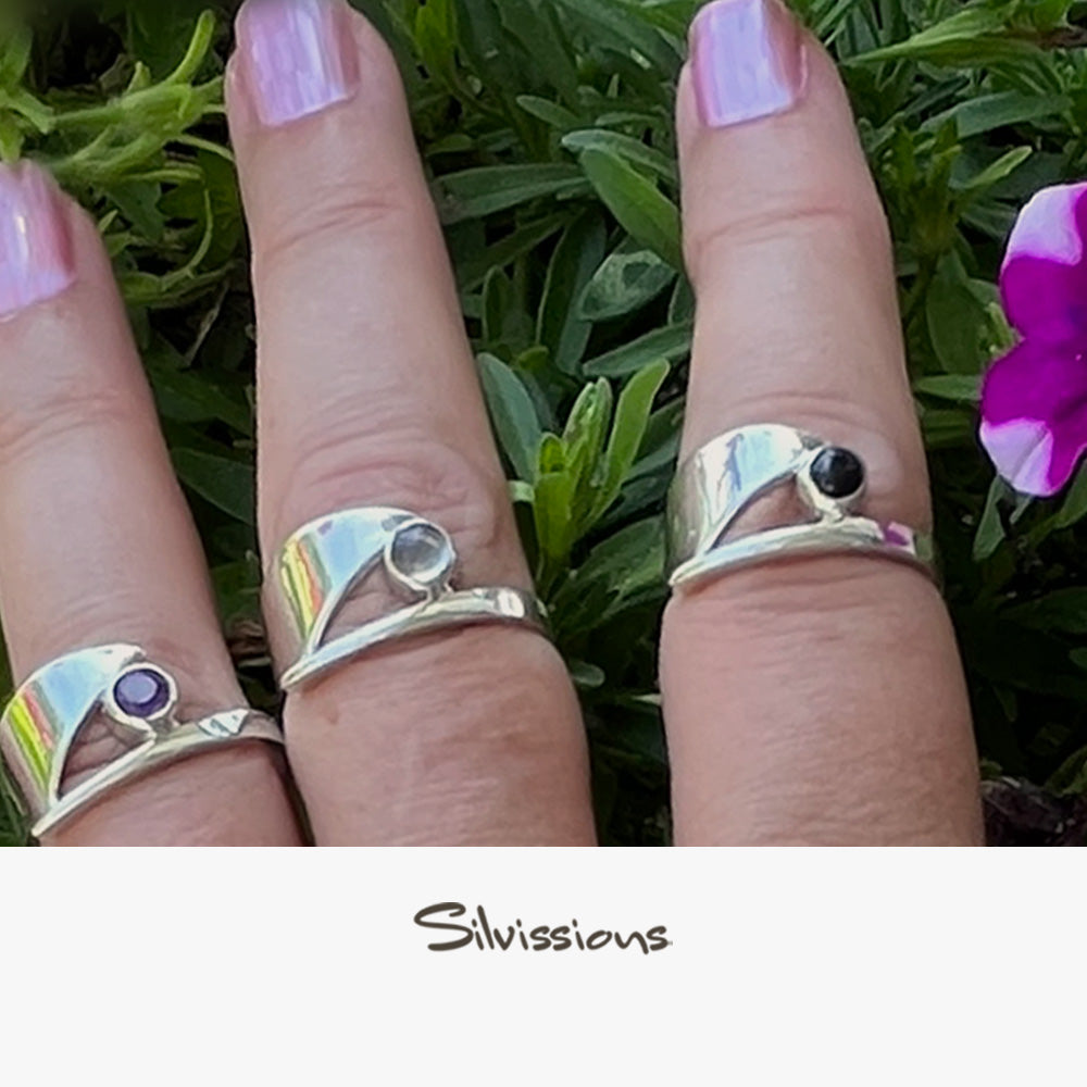 Three fingers wearing sterling silver rings with gemstones against a green leafy background, with 'Silvissions' branding.