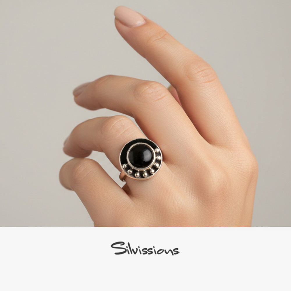 Hand wearing a black ring with silver accents on a neutral background, featuring the brand 'Silvissions'.