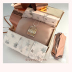 A square pendant necklace with a metallic gold tree design on a silver-toned rectangular frame, displayed inside an open gift box lined with star-patterned tissue paper. A rose gold pouch is visible to the right, and the brand name 'SILVISSIONS' is printed at the bottom.