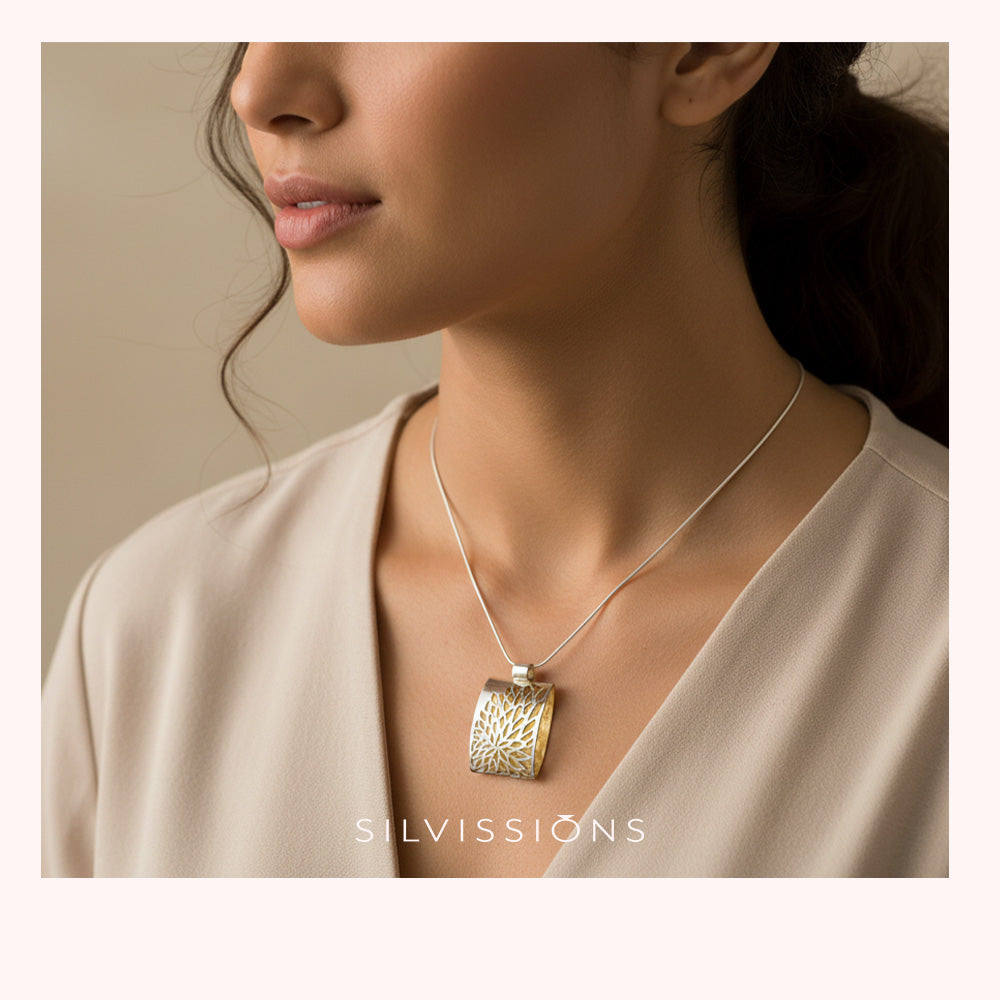 A close-up lifestyle shot of a model wearing a silver and gold pendant necklace. The pendant features a textured, openwork design with a silver body and gold accents, suspended from a delicate silver chain.