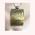 A silver-toned rectangular pendant necklace with a tree-of-life cutout design showing a gold-toned interior, suspended from a thin silver chain against a pale pink background. The brand name 'SILVISSIONS' is printed in red text below the pendant.
