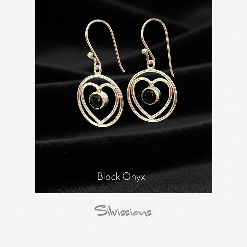 Heart-shaped earrings with black gemstones on a black background, branded 'Silvissions'.