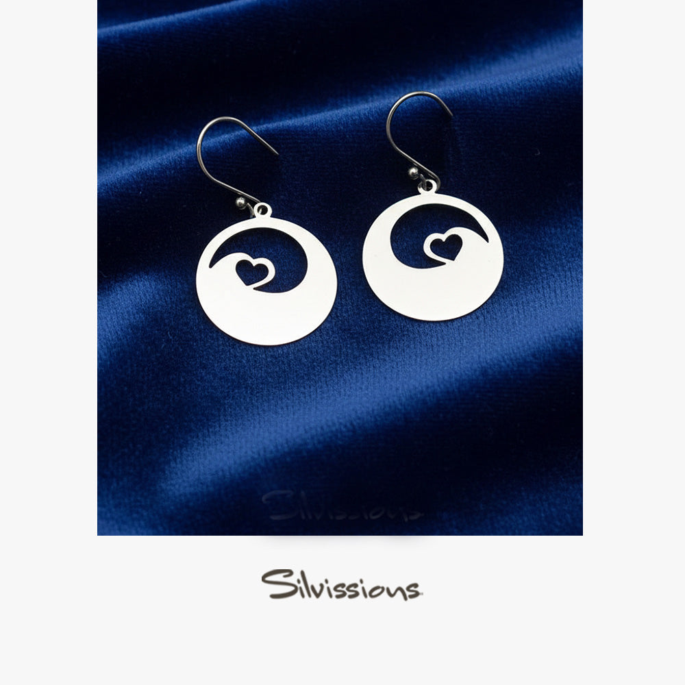 Silver earrings with heart design on a blue satin background, branded 'Silvissions'.