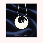 Silver necklace with a pendant featuring a heart design on a dark blue satin background, branded 'Silvissions'.