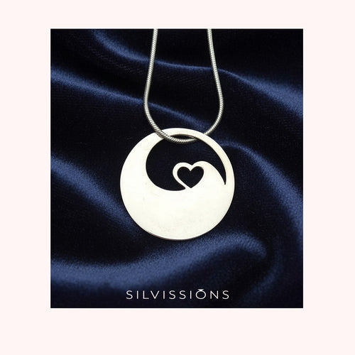 Silver necklace with a pendant featuring a heart design on a dark blue satin background, branded 'Silvissions'.