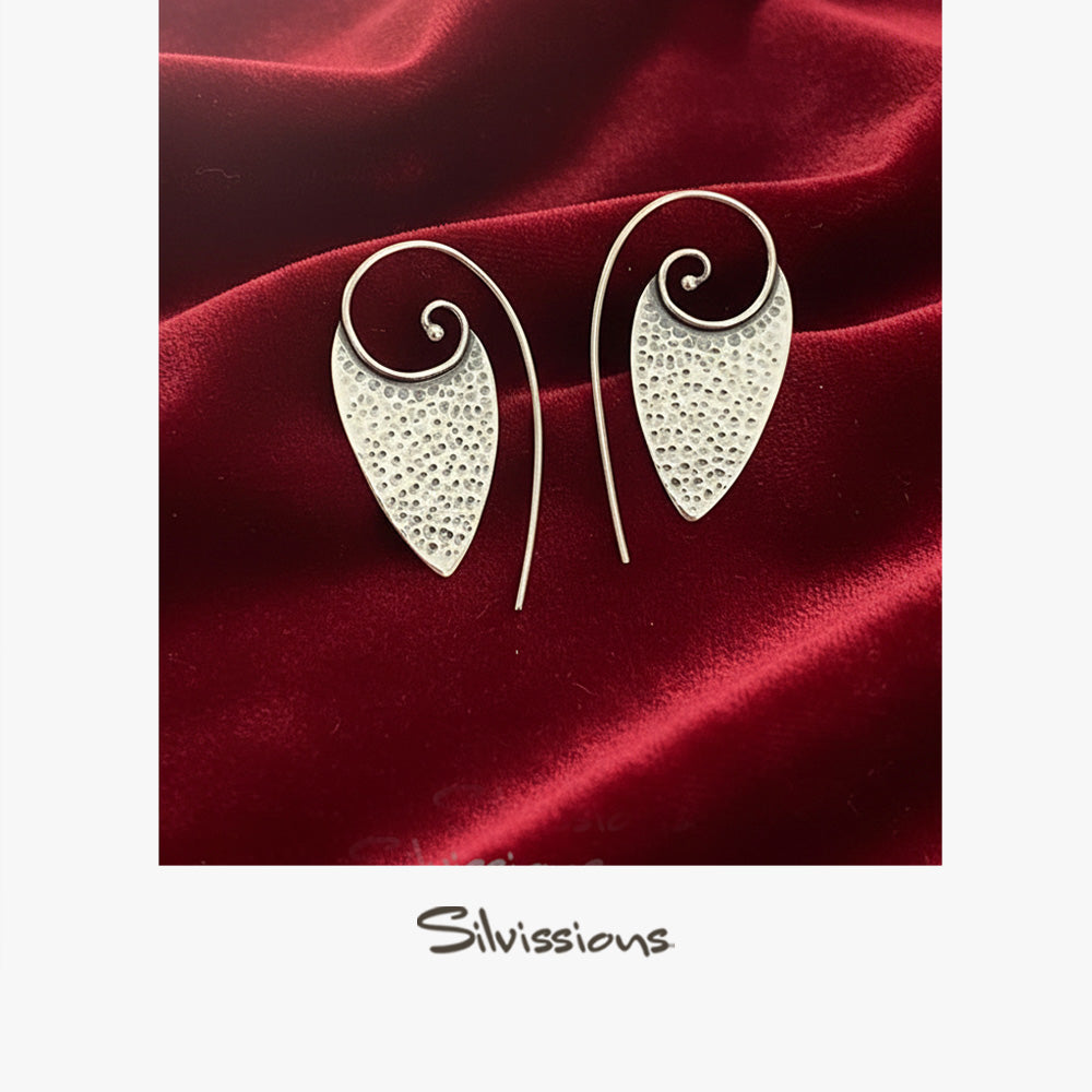 Silver earrings with intricate designs on a red fabric background, featuring the brand 'Silvissions'.