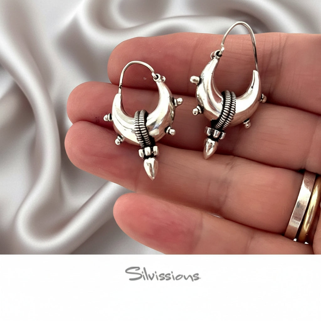 Silver earrings held in a hand with a white background, featuring the brand 'Silvissions'.