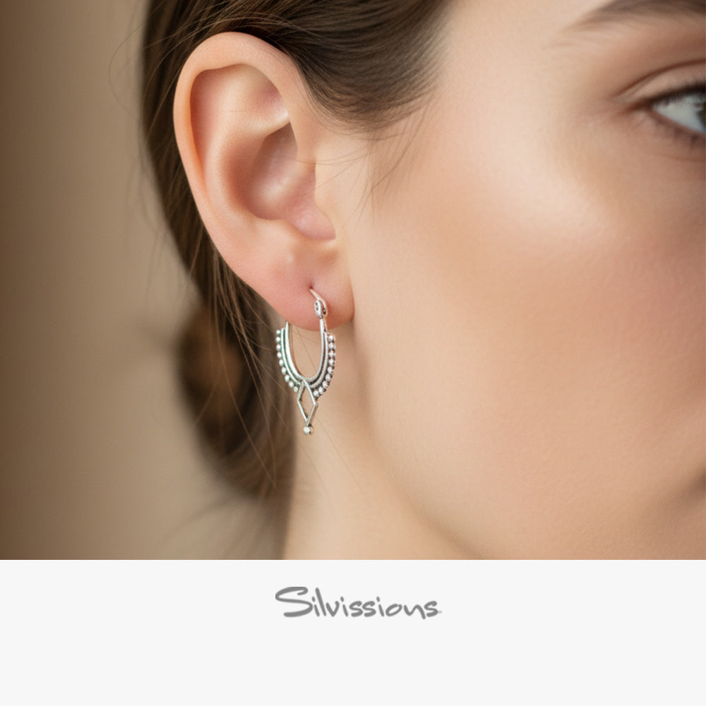 A close-up image of a woman's ear wearing a sterling silver hoop earring with intricate designs.
