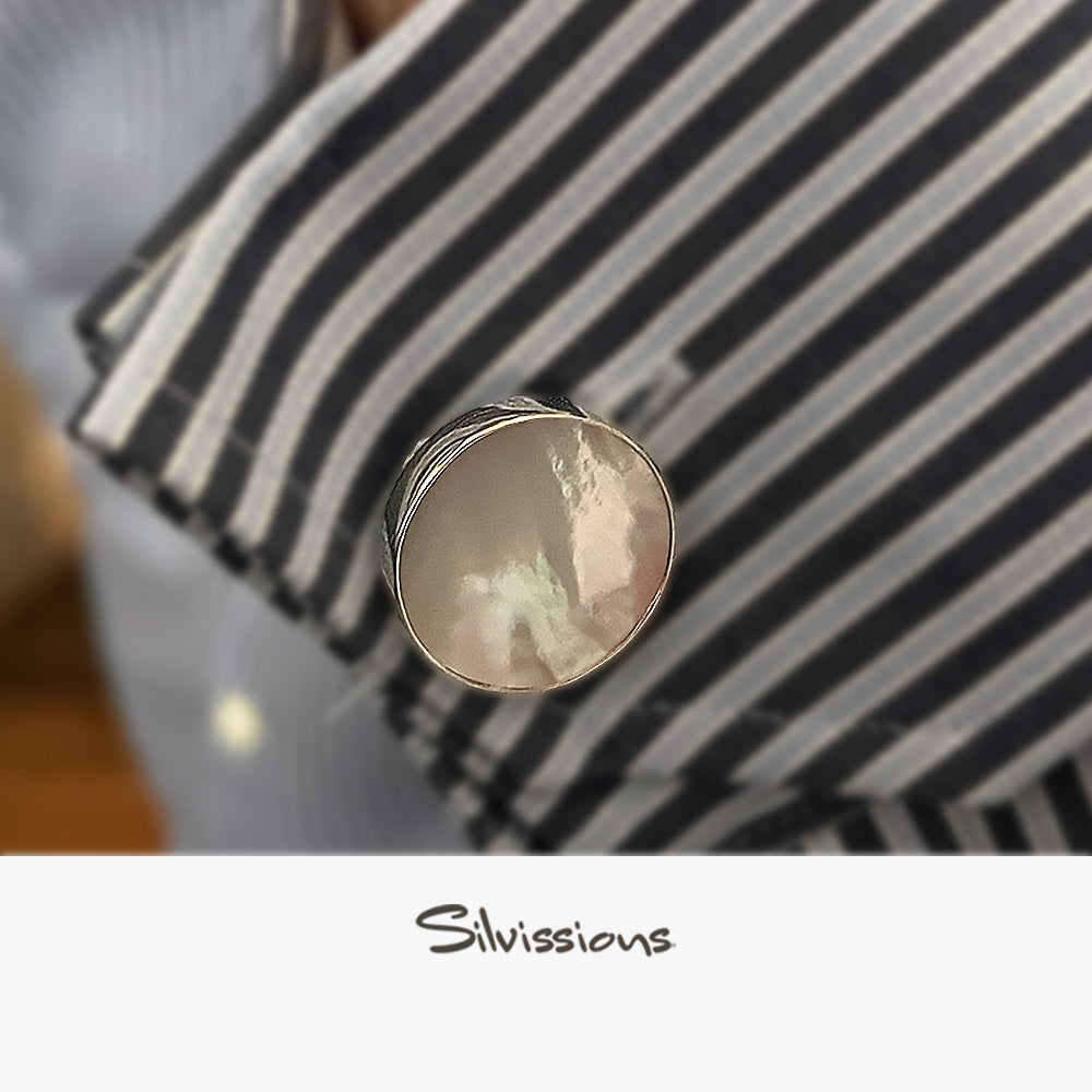Close-up of a silver cufflink with a mother of pearl gemstone on a striped fabric background, featuring the brand 'Silvissions'.