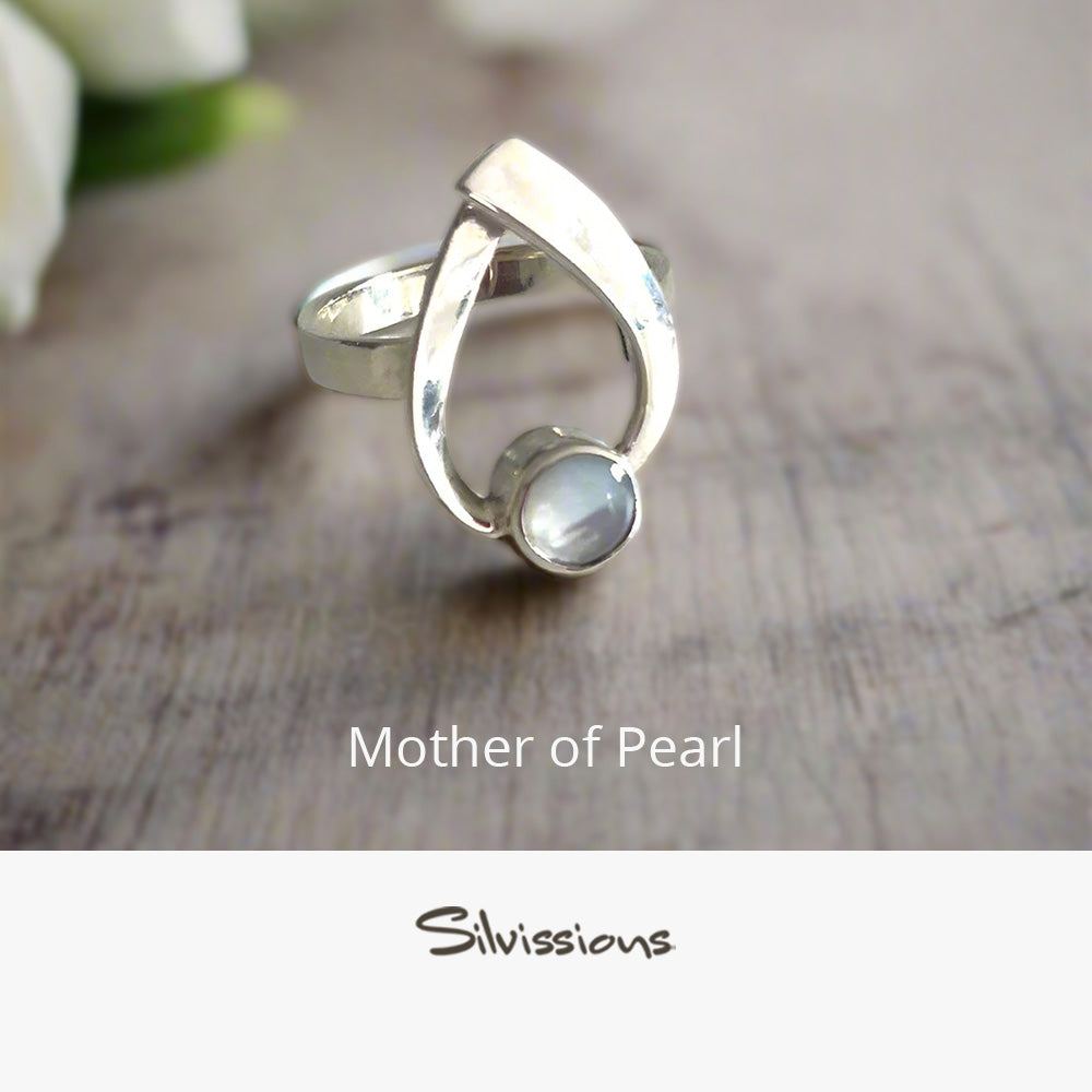 Silver ring with a mother of pearl stone on a wooden surface, branded 'Silvissions'.