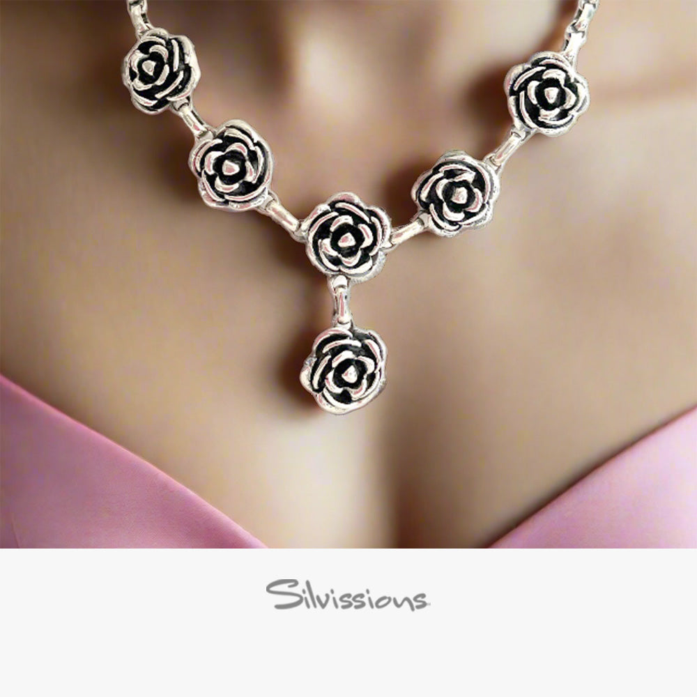 Silver rose necklace on a soft pink fabric background with 'Silvissions' branding.