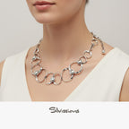 Silver necklace with circular links and small spheres worn by a person, brand 'Silvissions' visible.