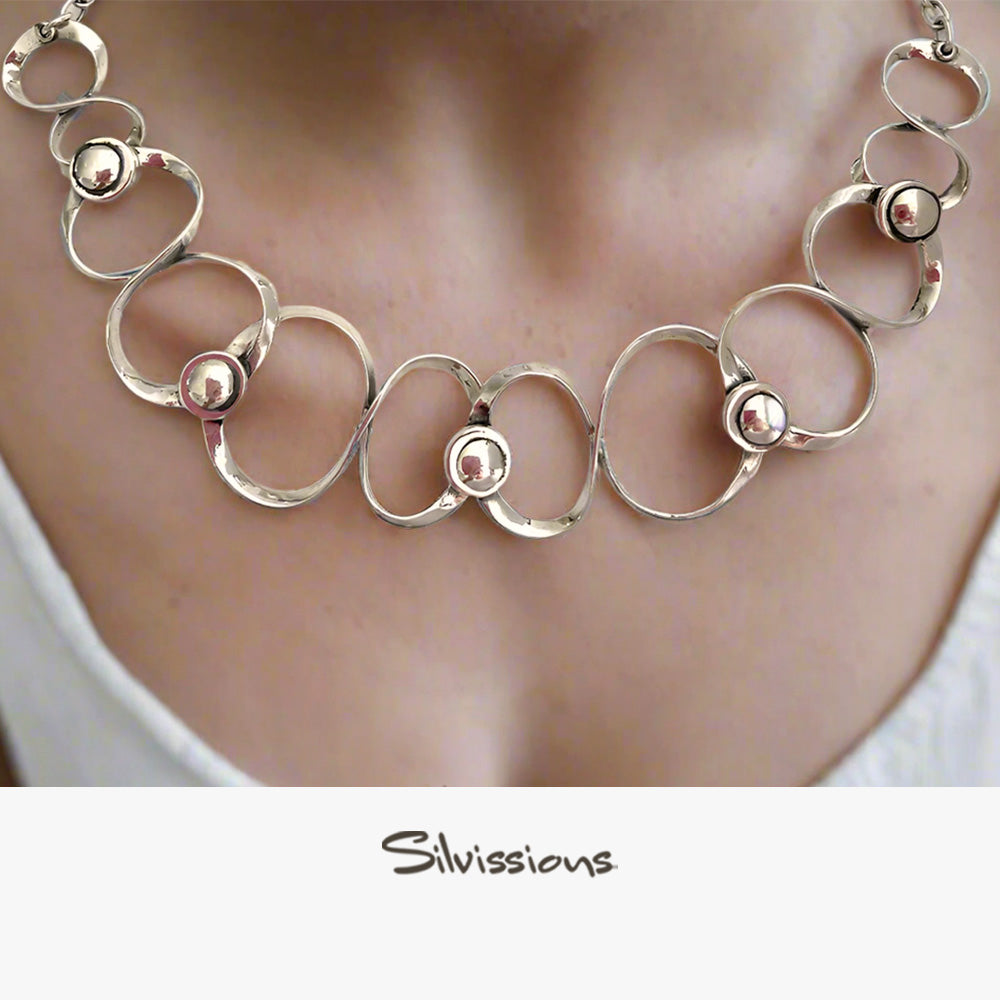 Silver necklace with circular links and small spheres worn by a person, brand 'Silvissions' visible.
