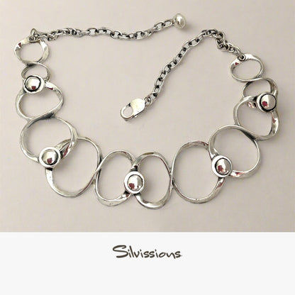 Silver necklace with circular links and embedded beads on a beige background, branded 'Silvissions'.