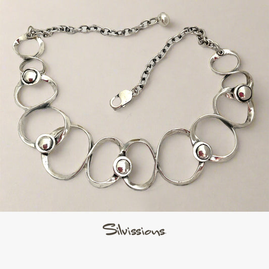 Silver necklace with circular links and embedded beads on a beige background, branded 'Silvissions'.