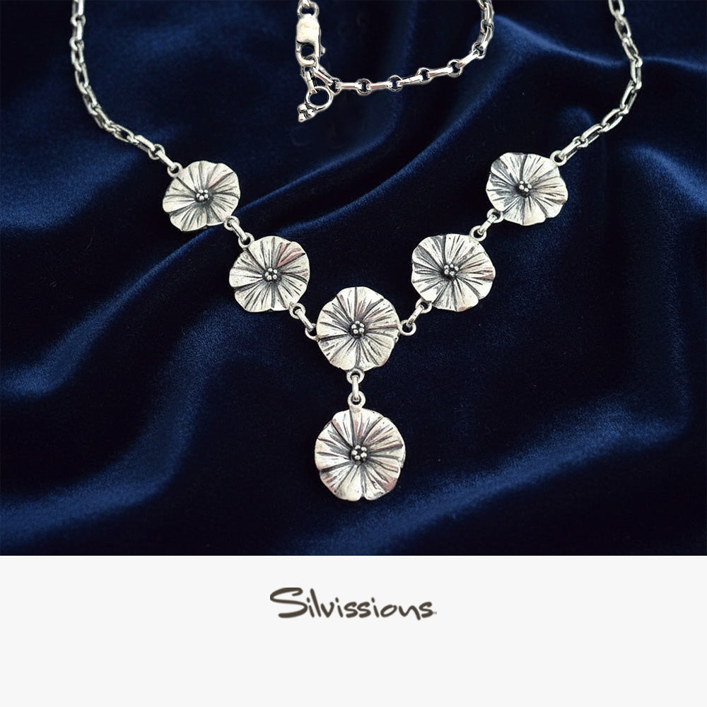 Silver necklace with floral pendants on a neutral background, branded 'Silvissions'.