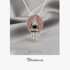 Jewelry pendant with black onyx gemstone and silver accents on a gray fabric background, branded 'Silvissions'.