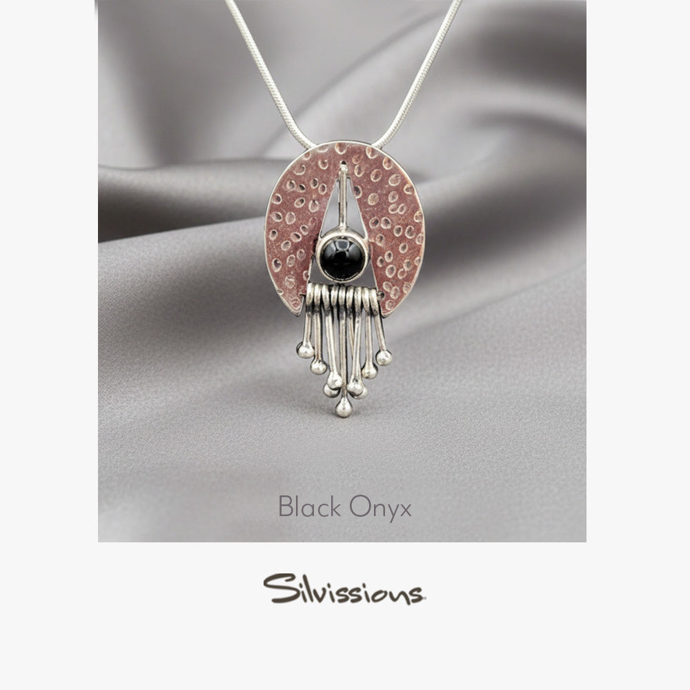 Jewelry pendant with black onyx gemstone and silver accents on a gray fabric background, branded 'Silvissions'.