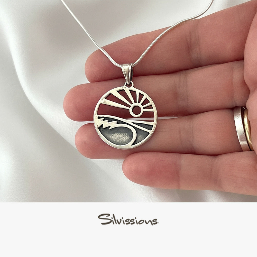 Silver pendant with a design held by a hand on a white background, branded 'Silvissions'.