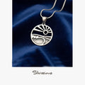 Silver pendant with a design on a blue fabric background, branded 'Silvissions'.