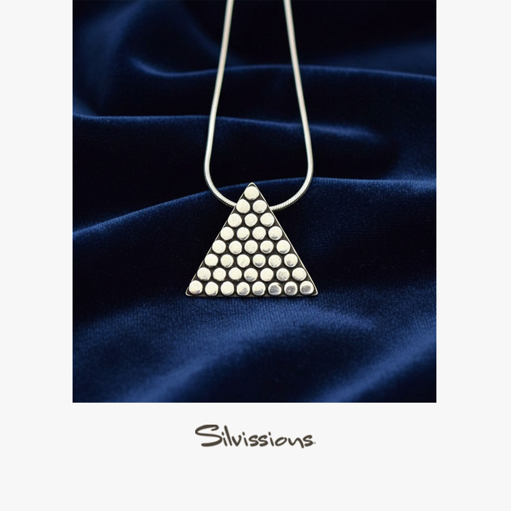 Triangular pendant necklace with metallic beads on a dark blue fabric background, branded 'Silvissions'.