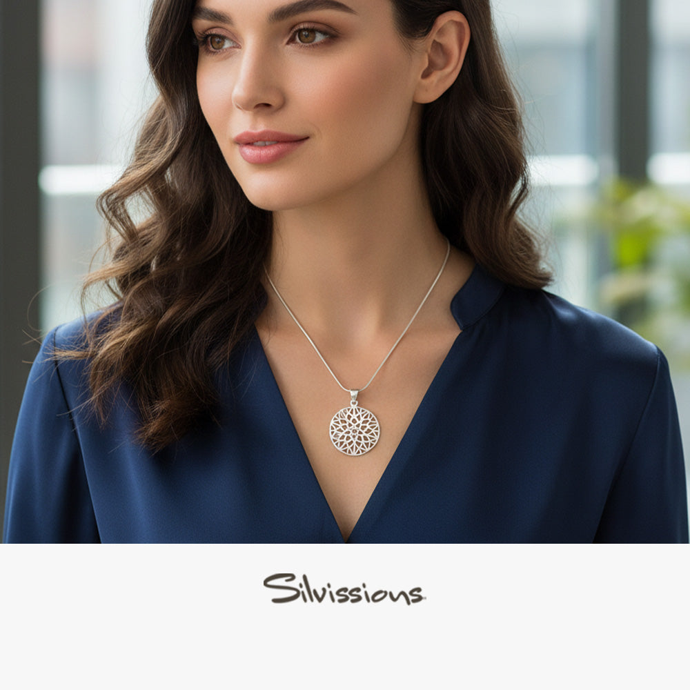 Woman wearing a silver necklace with a detailed pendant, set against a blurred indoor background.