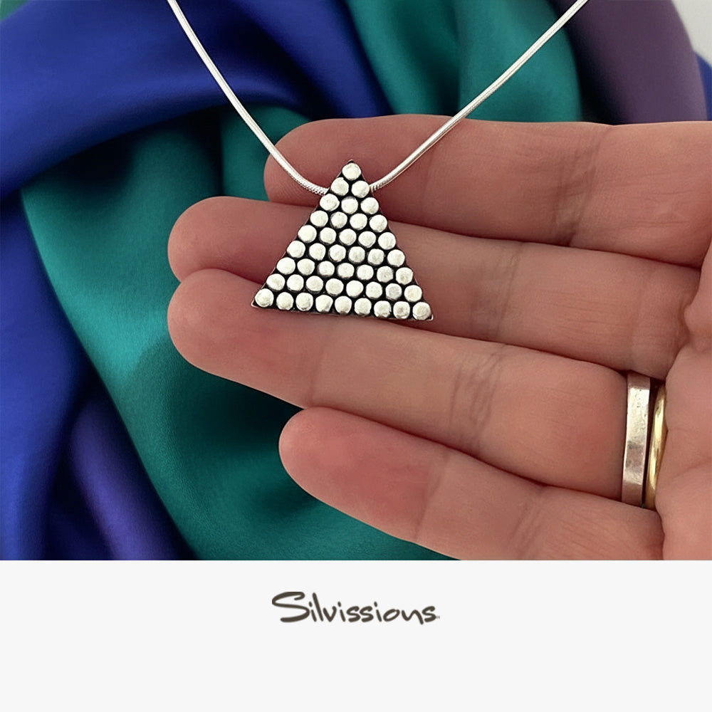 Triangular pendant held between fingers with colorful fabric background, featuring the brand 'Silvissions'.