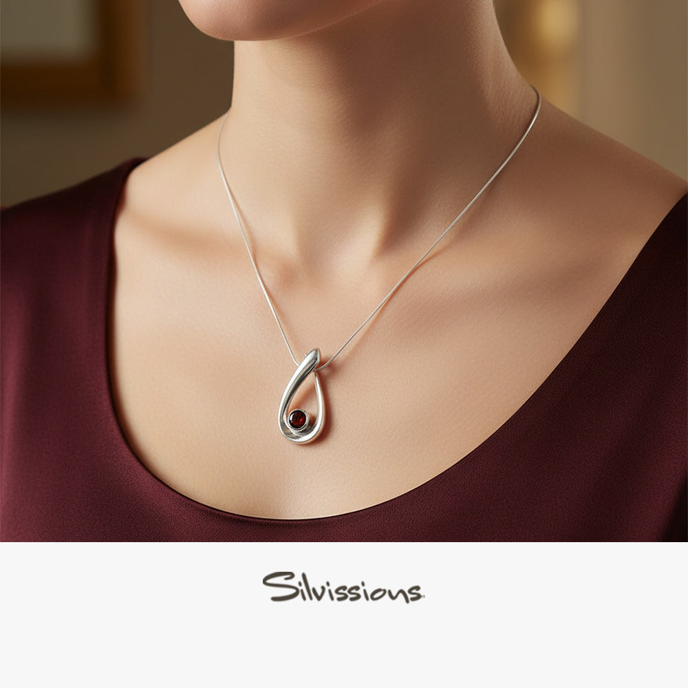 Necklace with a red garnet gemstone pendant on a woman wearing a burgundy top, branded 'Silvissions'.