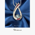 Silver pendant with blue gemstone on blue fabric, featuring 'Silvissions' brand.