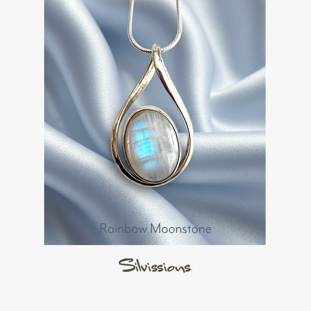Teardrop-shaped pendant with rainbow moonstone on a silver chain against a satin background, branded 'Silvassions'.