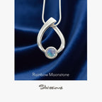 Silver pendant with rainbow moonstone on a blue satin background, featuring the brand 'Silvions'.