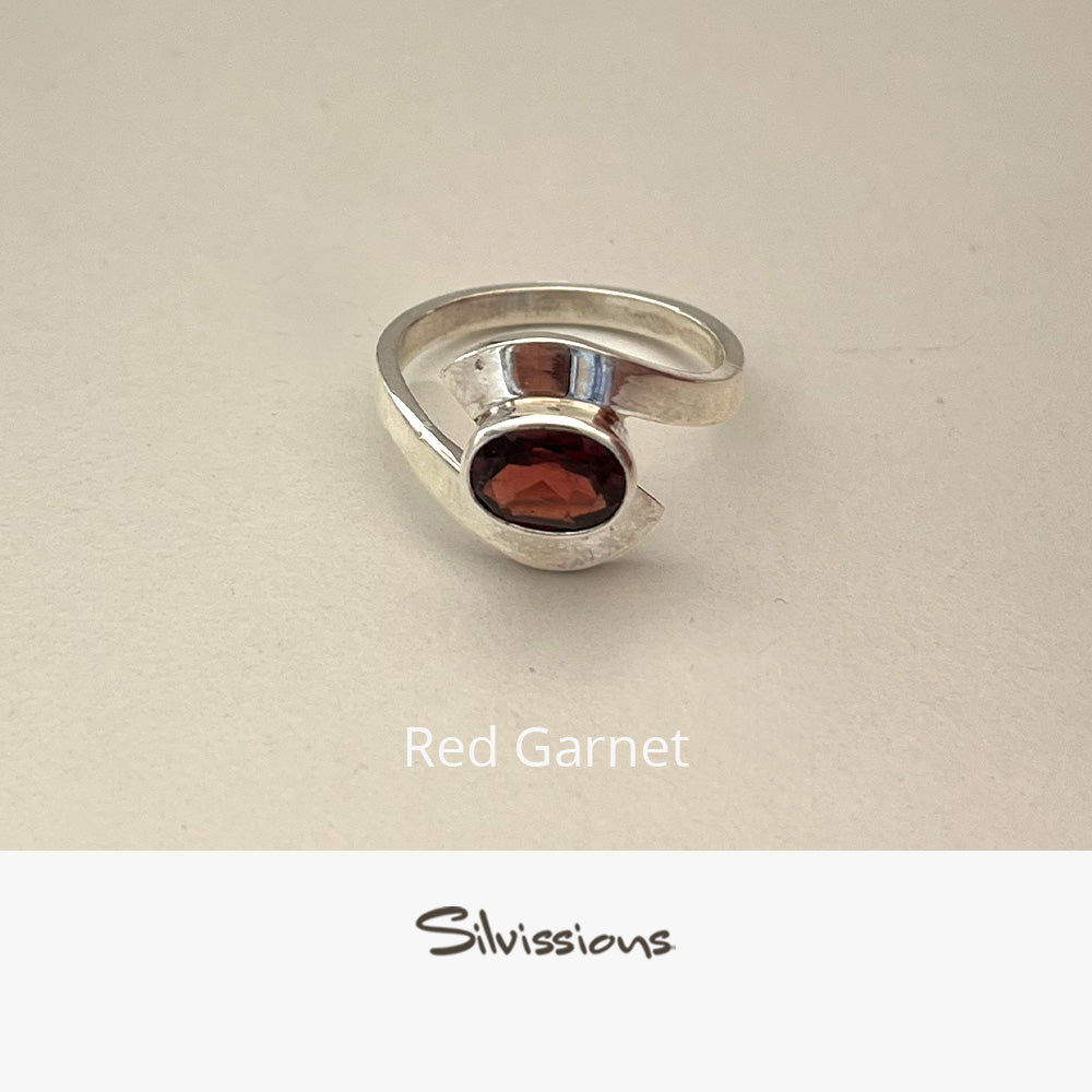 Silver ring with a red gemstone on a beige background, featuring the brand 'Silvissions'.