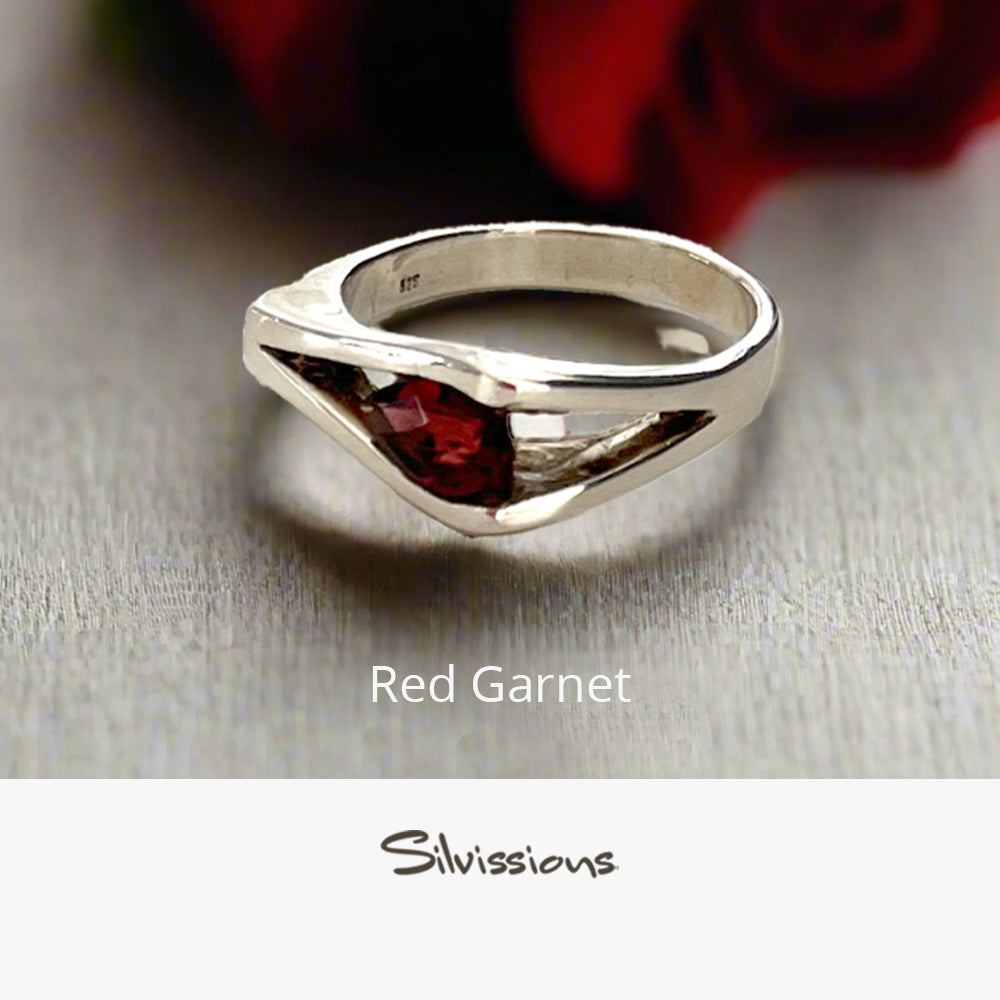 Silver ring with a red gemstone on a light wooden surface, branded 'Silvissions'.