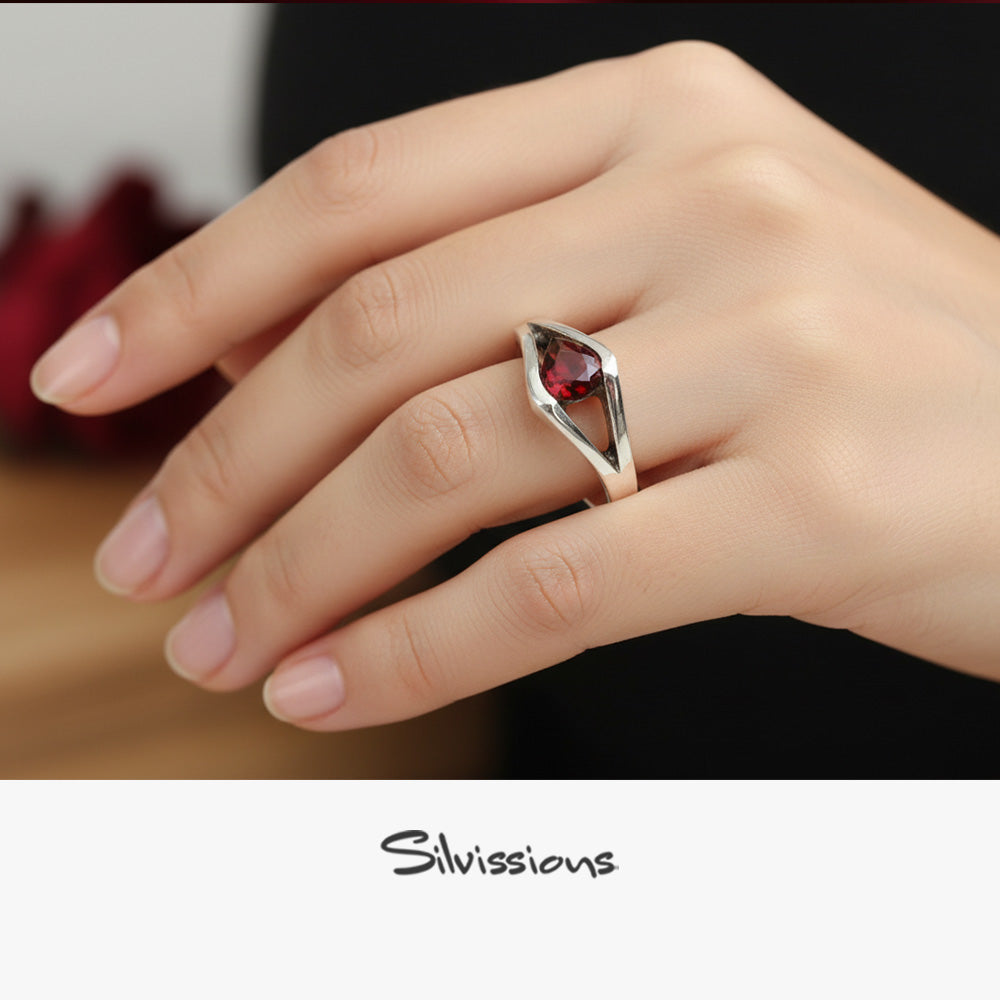 Hand wearing a silver ring with a red gemstone, brand 'Silvissions' visible
